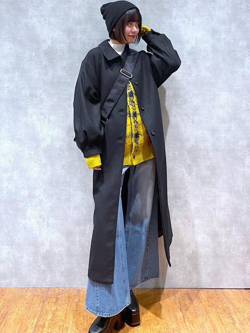 ブラック系のチェスターコート、ブルー系のデニムパンツ、イエロー系のカーディガン/ボレロを着用したレディースの冬コーディネートの1枚目の写真