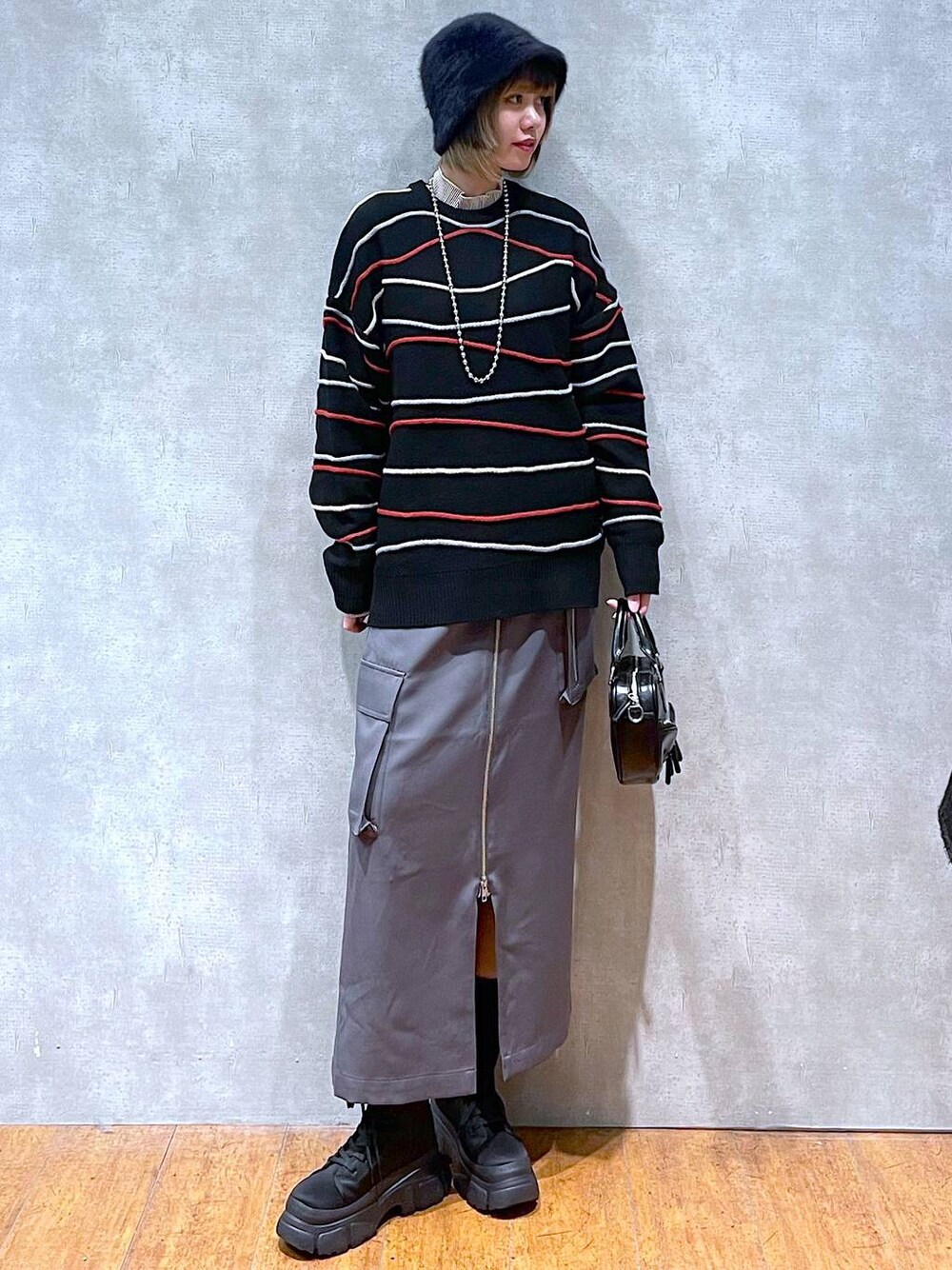 グレー系のスカート、ベージュ系のTシャツ/カットソー、ブラック系のニット/セーターを着用したレディースの冬コーディネートの1枚目の写真