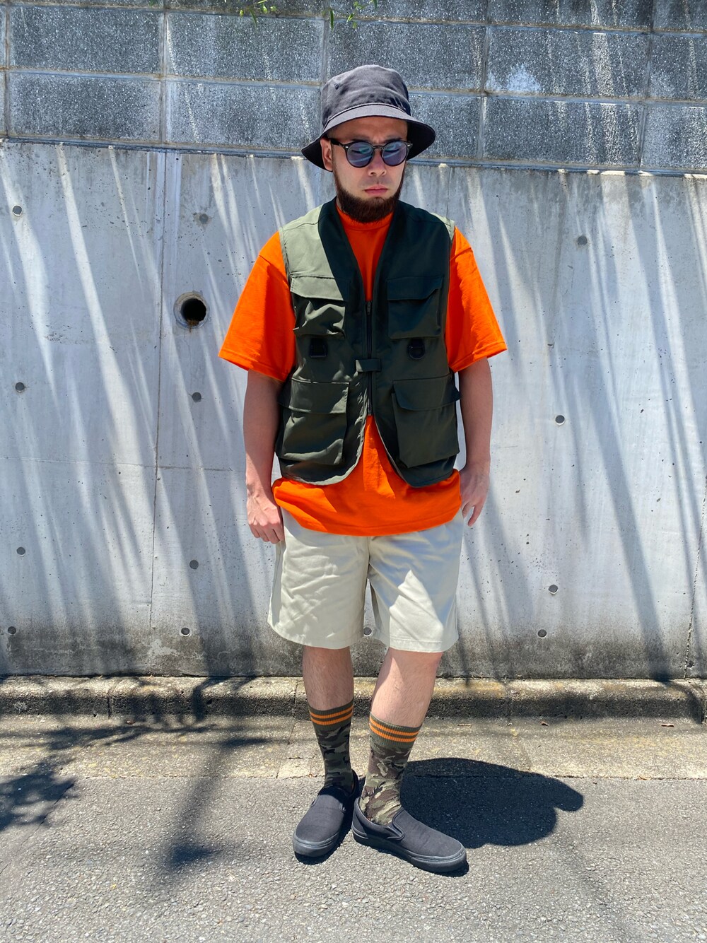 ブラック系のスリッポン、ベージュ系のパンツ、オレンジ系のTシャツ/カットソーを着用したメンズの夏コーディネートの1枚目の写真