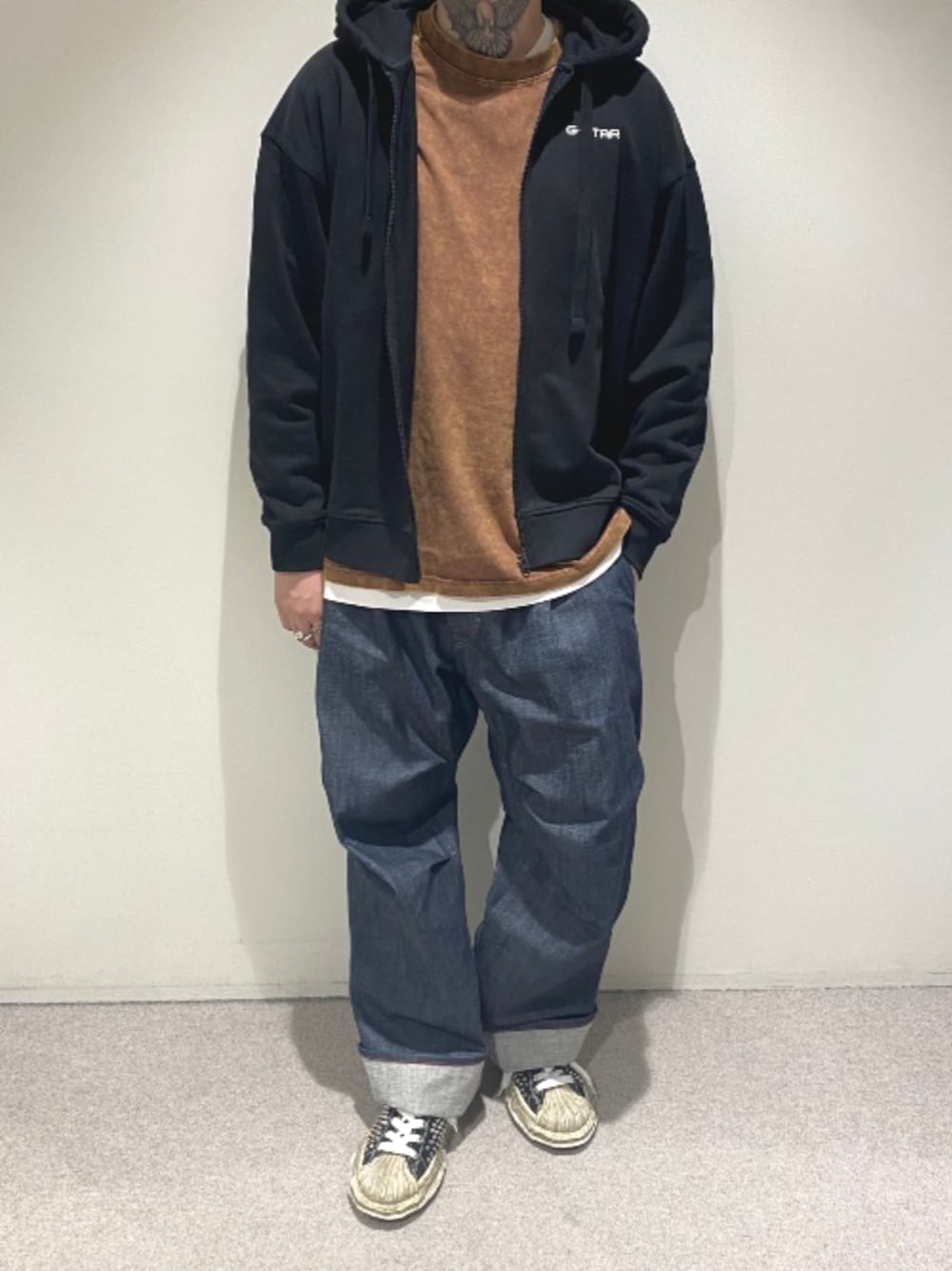 ブラック系のパーカー、ブラウン系のTシャツ/カットソー、ブルー系のデニムパンツを着用したメンズの秋コーディネートの1枚目の写真