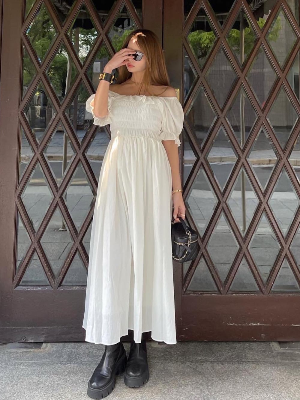 ホワイト系のワンピース、ブラック系のブーツ、ブラック系のショルダーバッグを着用したレディースの春コーディネートの1枚目の写真