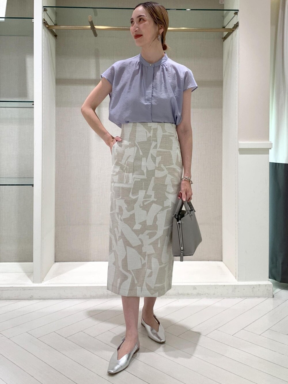 グレー系のハンドバッグ、シルバー系のパンプス、ベージュ系のスカートを着用したレディースの夏コーディネートの1枚目の写真