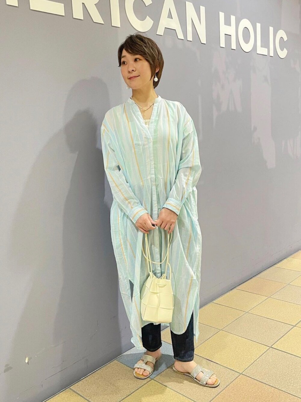 ホワイト系のショルダーバッグ、ブルー系のデニムパンツ、ブルー系のワンピースを着用したレディースの春コーディネートの1枚目の写真