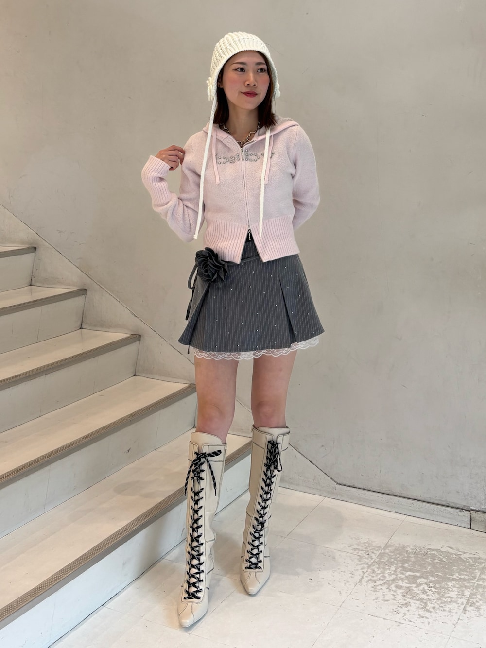 ピンク系のパーカー、グレー系のスカート、ホワイト系のブーツを着用したレディースの冬コーディネートの1枚目の写真