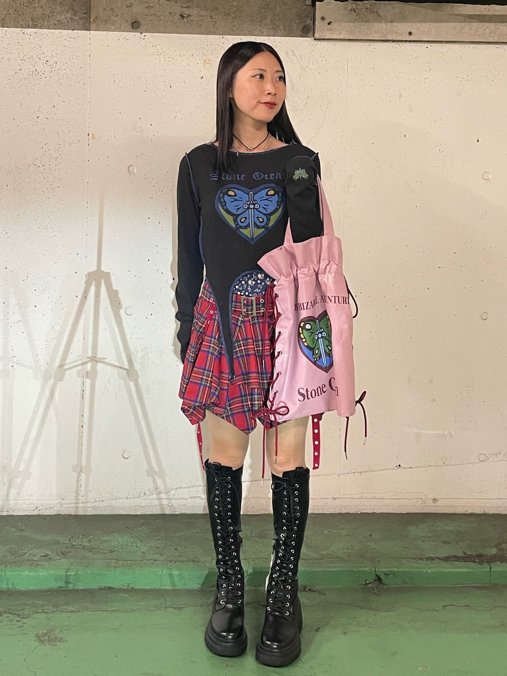 レッド系のスカート、ブラック系のブーツ、ブラック系のTシャツ/カットソーを着用したレディースの秋コーディネートの1枚目の写真