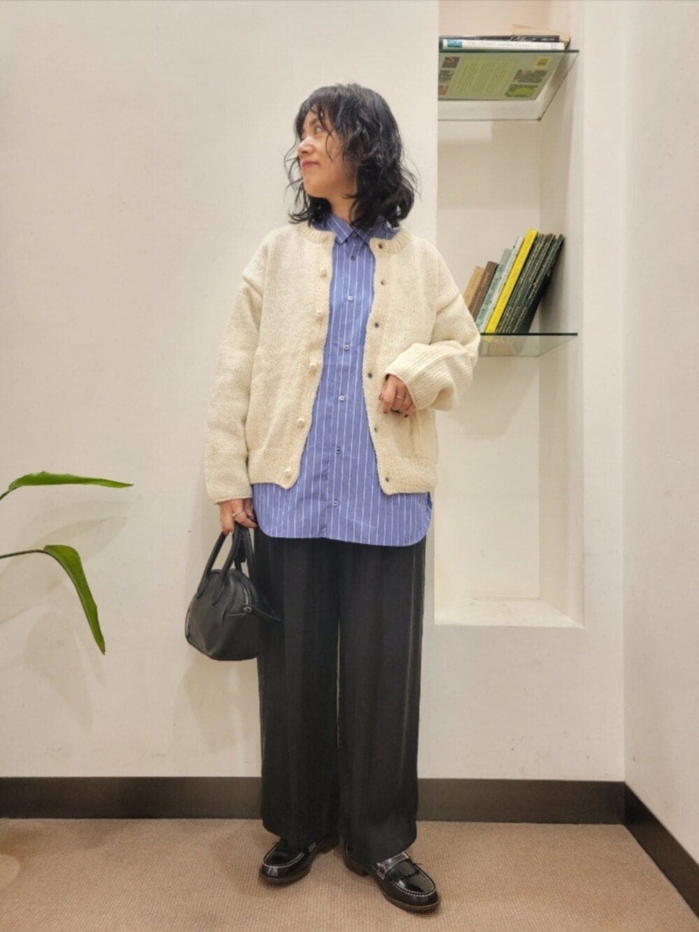 ブラック系のハンドバッグ、ブラック系のローファー、ホワイト系のニット/セーターを着用したレディースの秋コーディネートの1枚目の写真