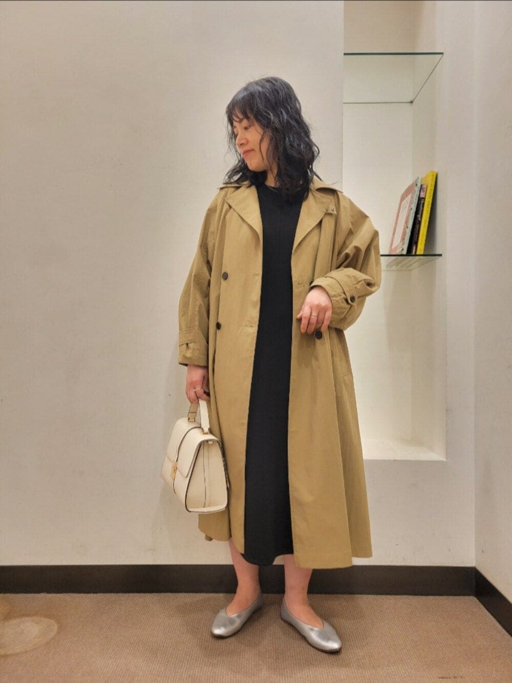 ベージュ系のトレンチコート、ブラック系のワンピース、シルバー系のパンプスを着用したレディースの冬コーディネートの1枚目の写真