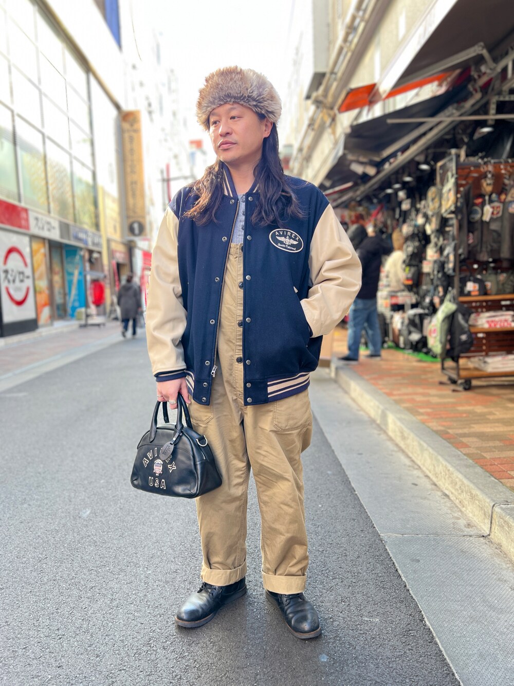 ブルー系のスタジャン、ブラック系のボストンバッグ、グリーン系のキャップを着用したメンズの冬コーディネートの1枚目の写真