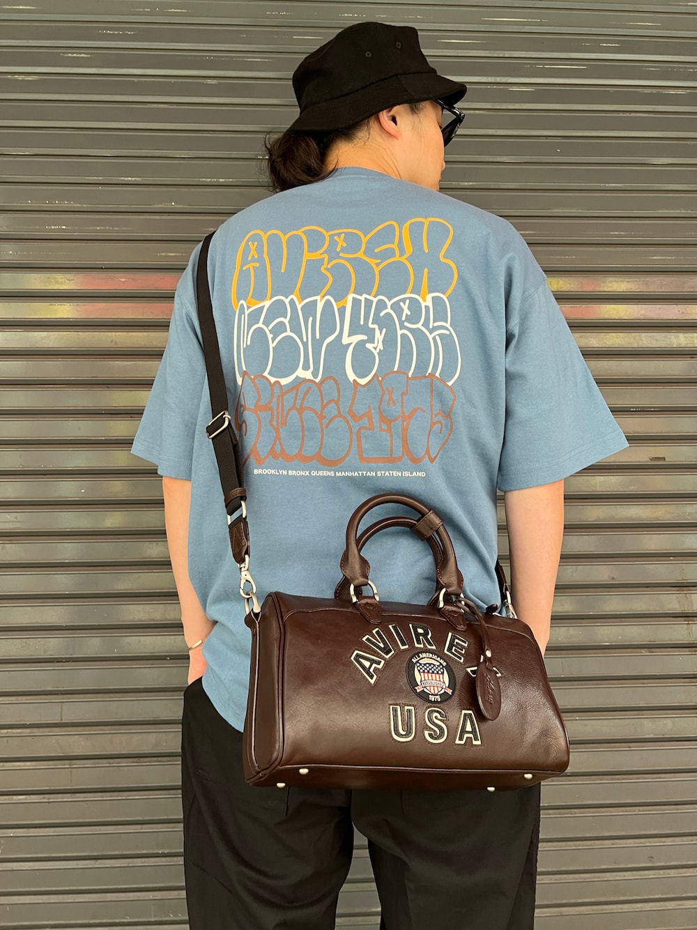 グレー系のTシャツ/カットソー、ブラウン系のボストンバッグ、ブラック系のハットを着用したメンズの夏コーディネートの1枚目の写真