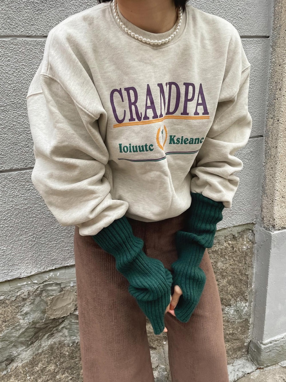 ベージュ系のスウェット、ブラウン系のスラックス、グリーン系のアームカバーを着用したレディースの冬コーディネートの1枚目の写真