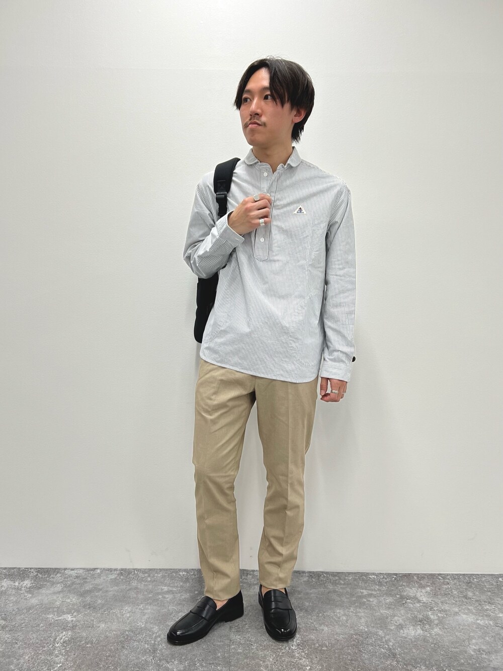 ブラック系のシャツ/ブラウス、ベージュ系のチノパンツ、ブラック系のバックパック/リュックを着用したメンズの春コーディネートの1枚目の写真