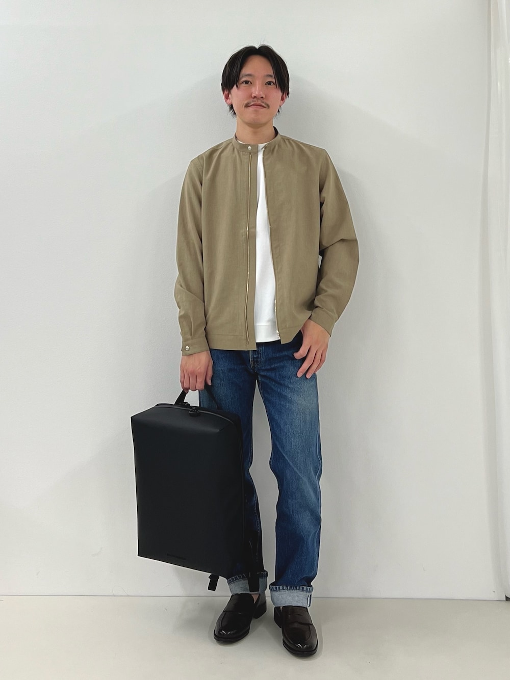 ホワイト系のTシャツ/カットソー、ベージュ系のブルゾン、ブラック系のバックパック/リュックを着用したメンズの春コーディネートの1枚目の写真