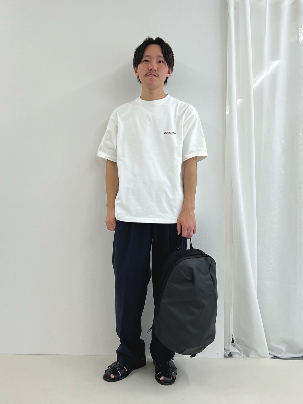 ホワイト系のTシャツ/カットソー、グレー系のバックパック/リュック、ブラック系のその他パンツを着用したメンズの春コーディネートの1枚目の写真