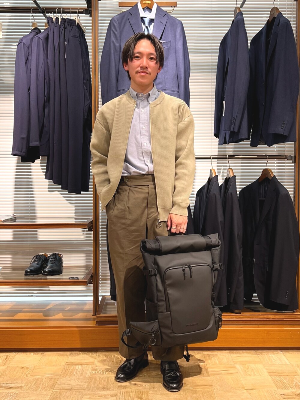 ベージュ系のカーディガン/ボレロ、ブラック系のバックパック/リュック、ブラック系のローファーを着用したメンズの春コーディネートの1枚目の写真