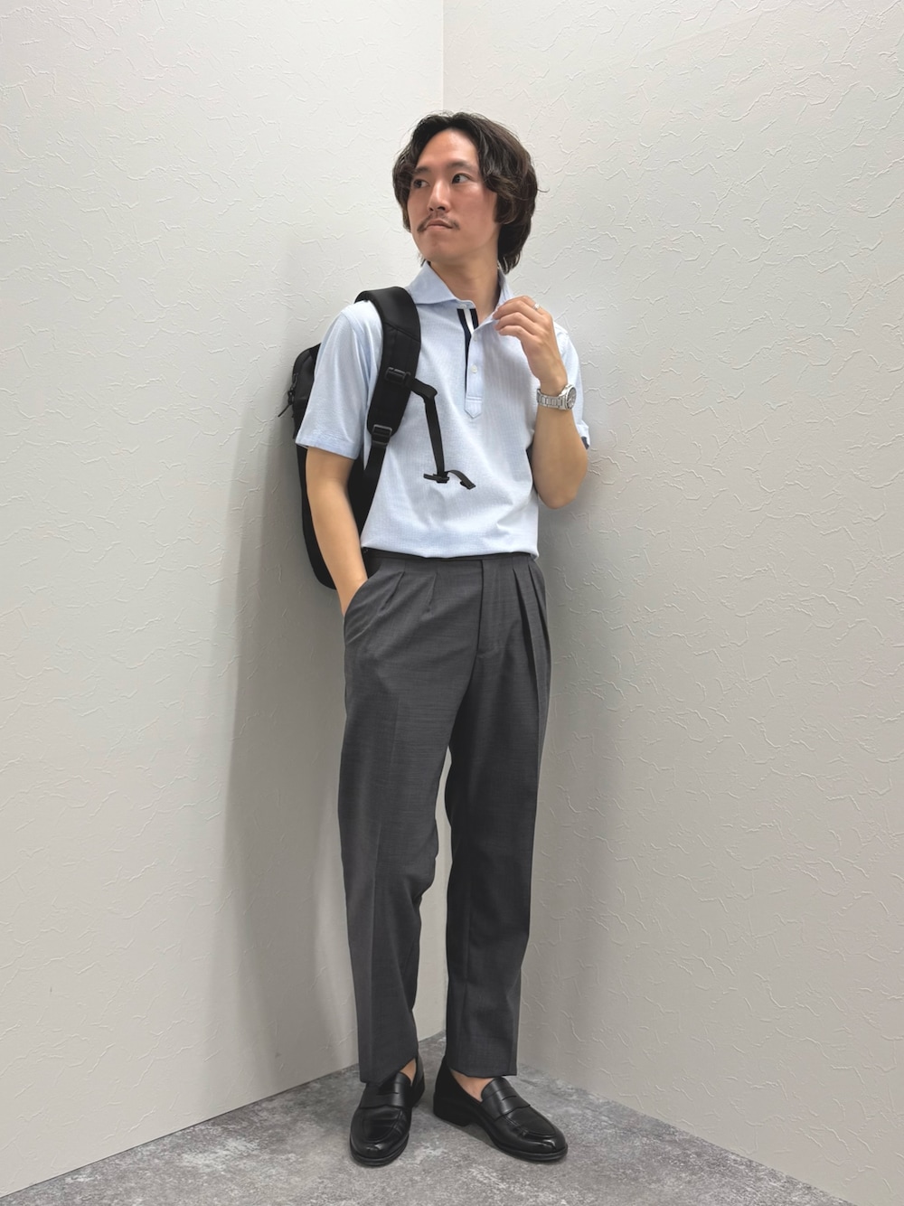 ブルー系のポロシャツ、グレー系のスラックス、ブラック系のバックパック/リュックを着用したメンズの春コーディネートの1枚目の写真