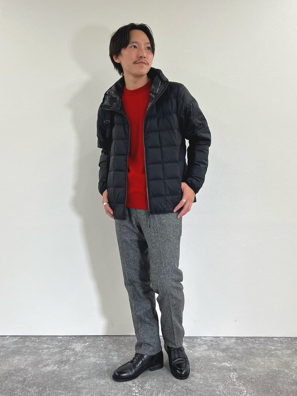 ブラック系のダウンジャケット/コート、レッド系のニット/セーター、グレー系のスラックスを着用したメンズの秋コーディネートの1枚目の写真