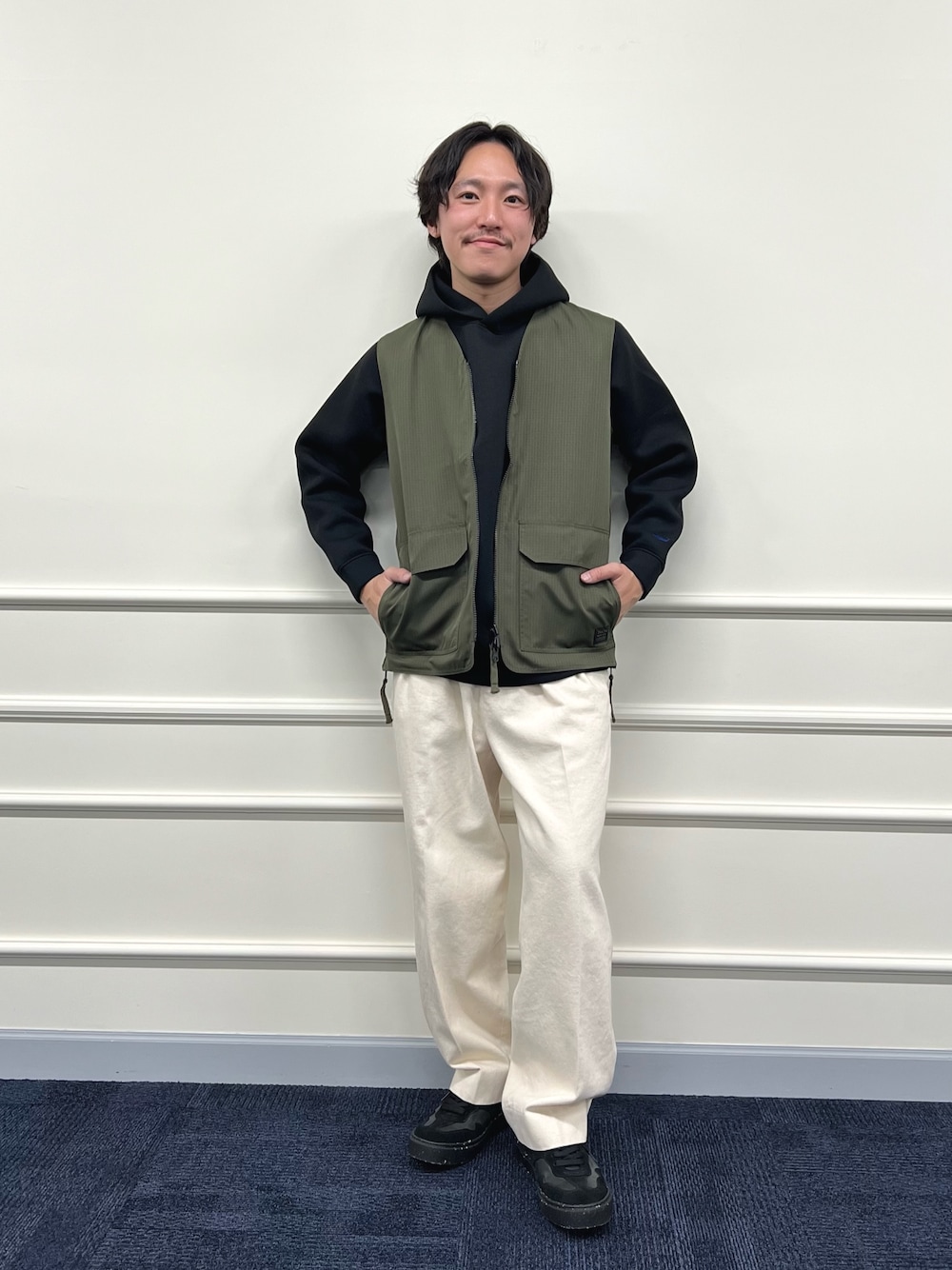 グリーン系のベスト、ブラック系のパーカー、ホワイト系のデニムパンツを着用したメンズの冬コーディネートの1枚目の写真