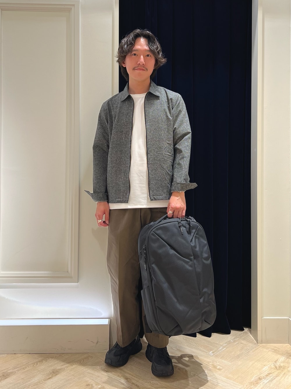 グレー系のブルゾン、ホワイト系のTシャツ/カットソー、ブラック系のバックパック/リュックを着用したメンズの春コーディネートの1枚目の写真