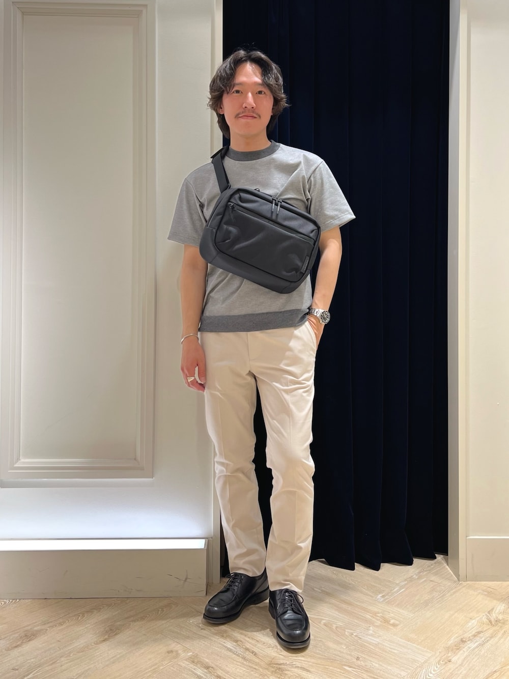 グレー系のTシャツ/カットソー、ブラック系のショルダーバッグ、ホワイト系のチノパンツを着用したメンズの春コーディネートの1枚目の写真