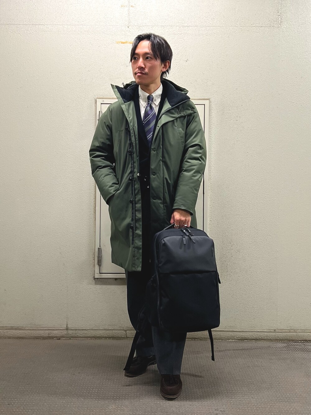 ブルー系のネクタイ、ブラック系のテーラードジャケット、グリーン系のダウンジャケット/コートを着用したメンズの冬コーディネートの1枚目の写真