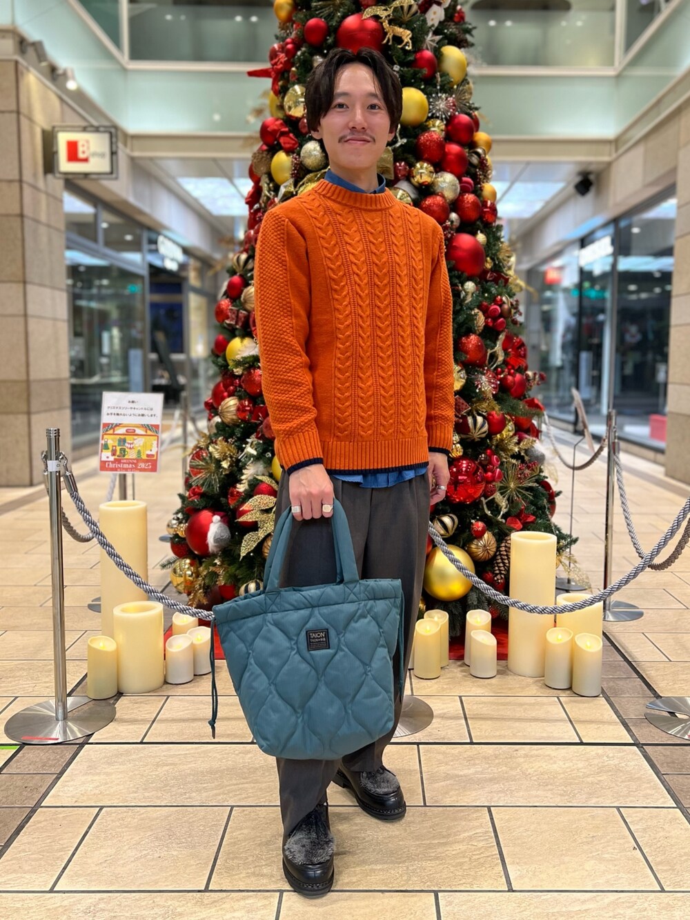 オレンジ系のニット/セーター、ブルー系のシャツ/ブラウス、グリーン系のトートバッグを着用したメンズの冬コーディネートの1枚目の写真