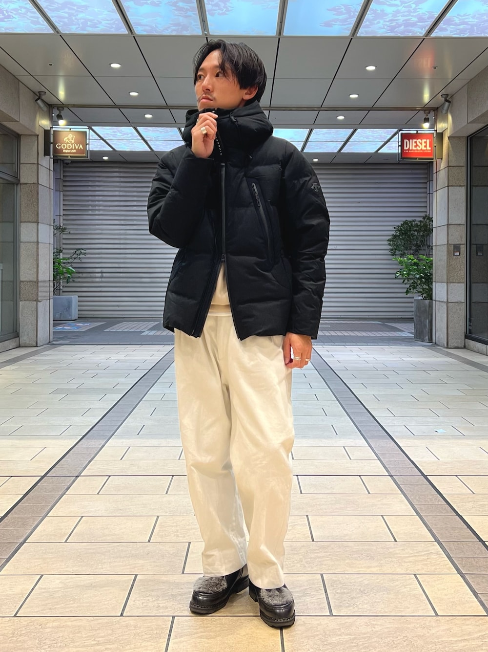 ベージュ系のトートバッグ、ベージュ系のTシャツ/カットソー、ブラック系のダウンジャケット/コートを着用したメンズの秋コーディネートの1枚目の写真