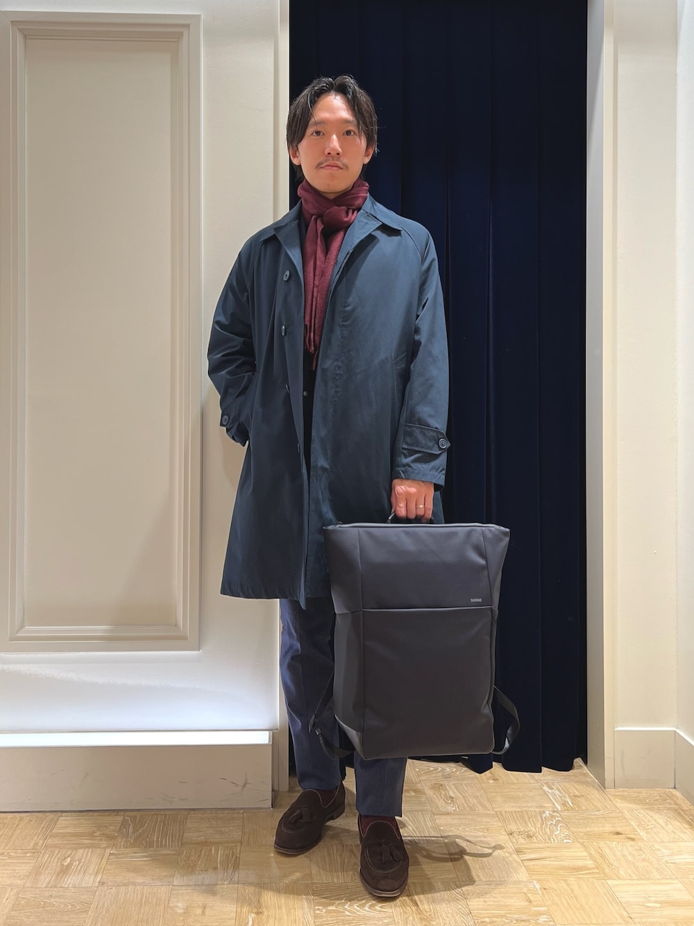 ブルー系のステンカラーコート、ブルー系のその他パンツ、ブラック系のバックパック/リュックを着用したメンズの冬コーディネートの1枚目の写真