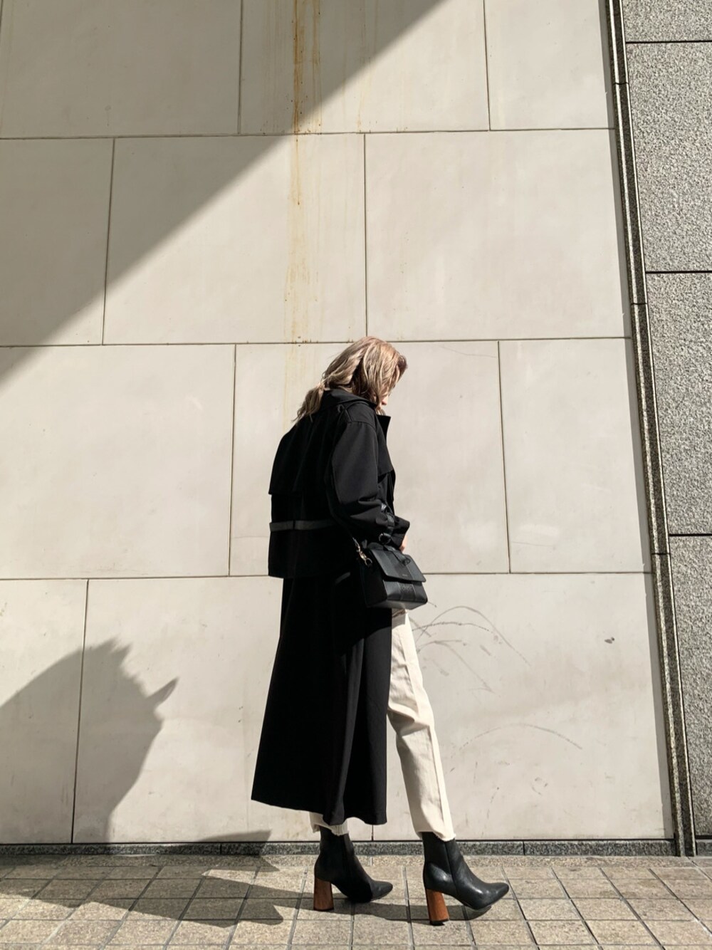 ブラック系のショルダーバッグ、ブラック系のトレンチコート、ホワイト系のデニムパンツを着用したレディースの冬コーディネートの1枚目の写真