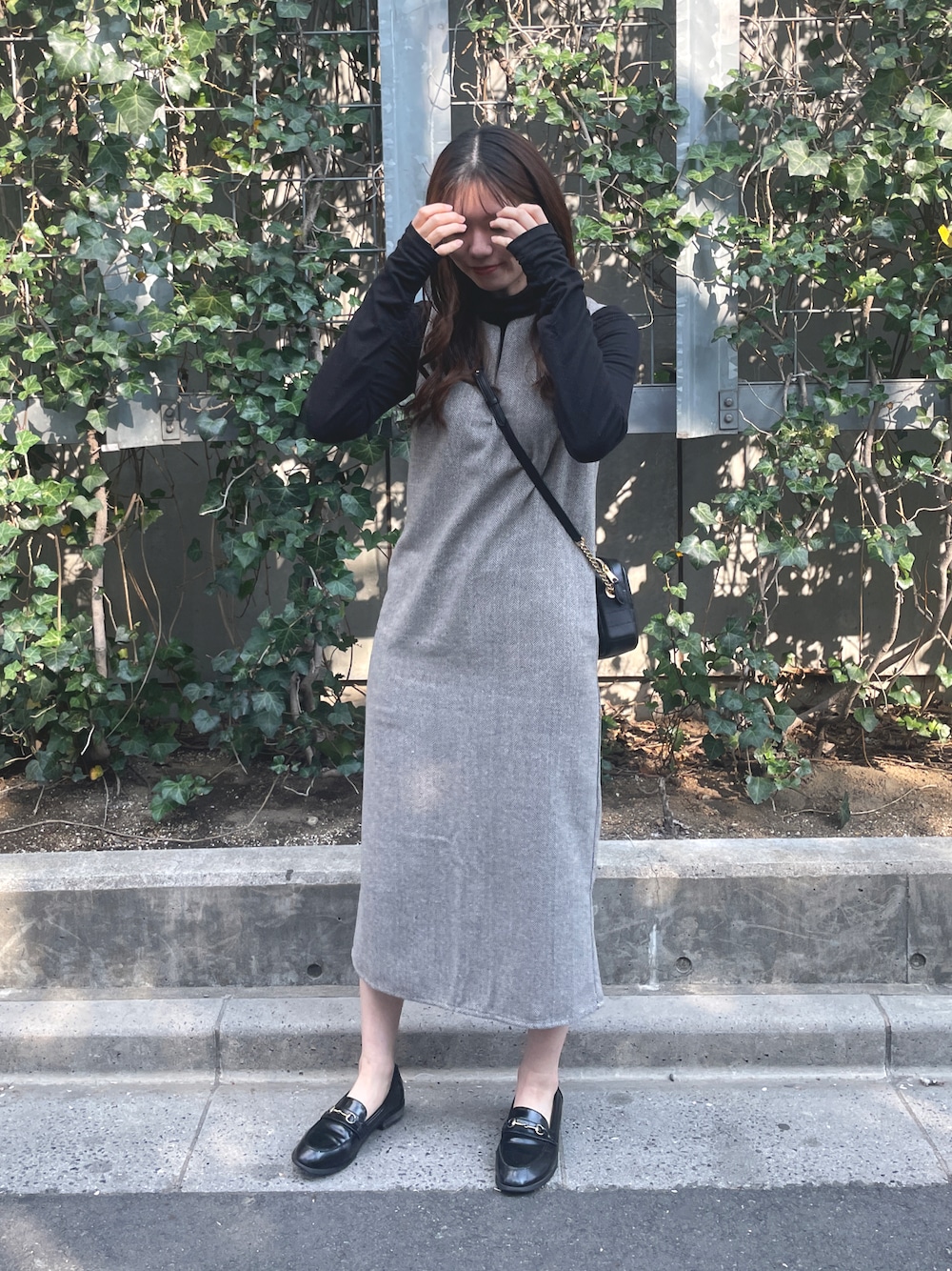 グレー系のジャンパースカート、ブラック系のショルダーバッグ、ブラック系のローファーを着用したレディースの春コーディネートの1枚目の写真