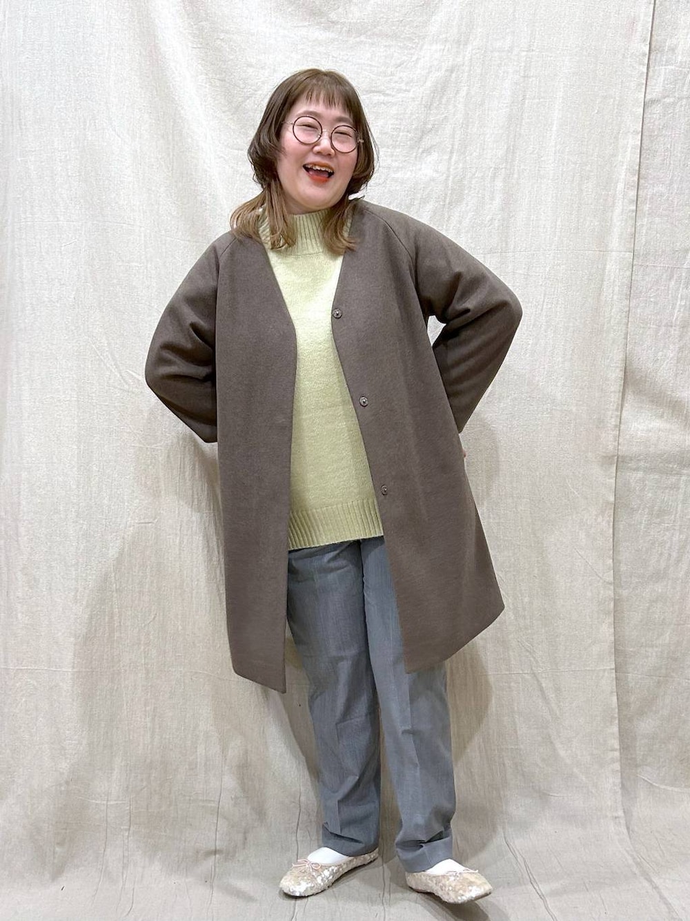 ブラウン系のノーカラーコート、グリーン系のニット/セーター、その他のその他パンツを着用したレディースの冬コーディネートの1枚目の写真