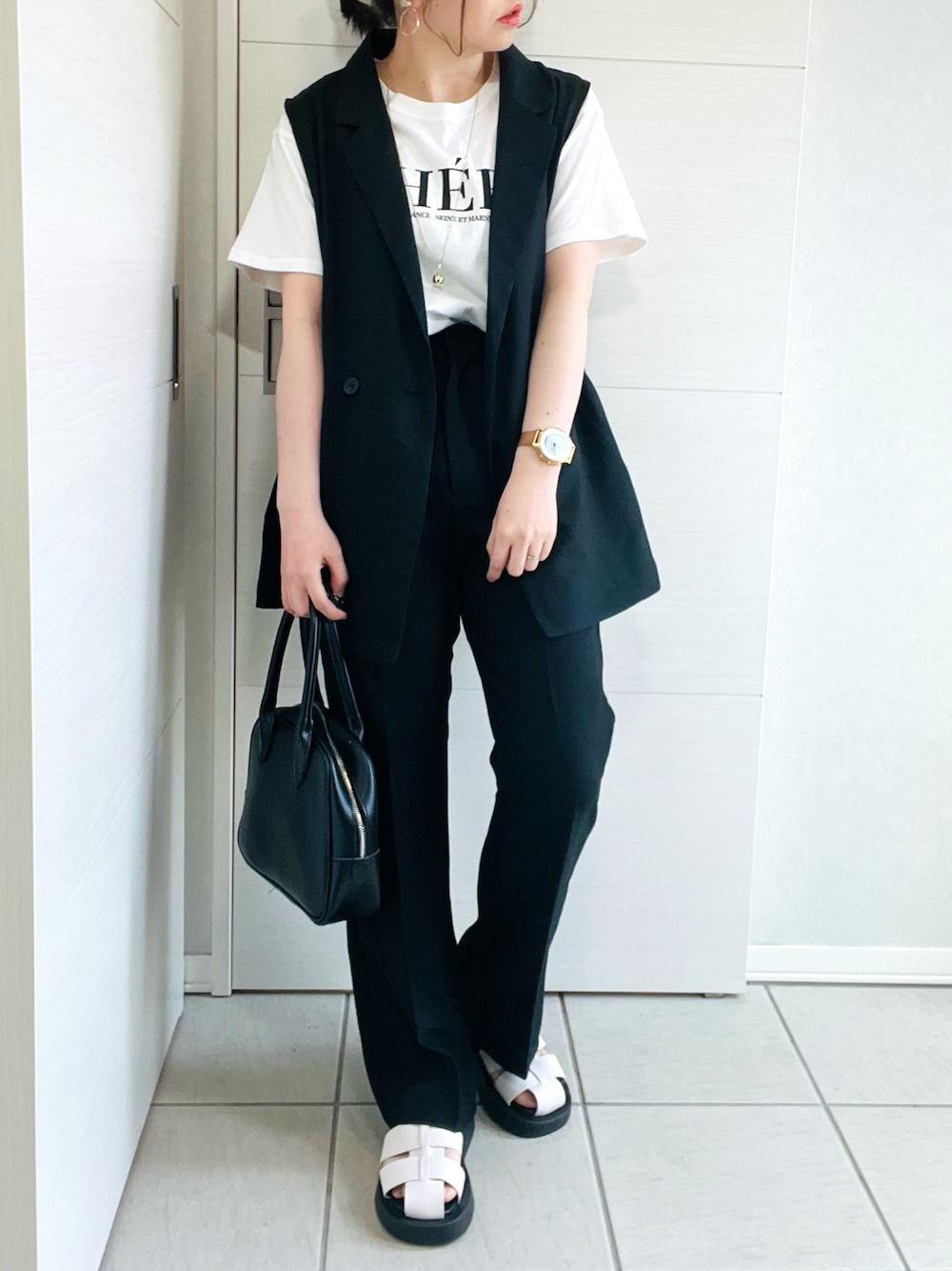 ブラック系のベスト、ホワイト系のTシャツ/カットソー、ブラック系のスラックスを着用したレディースの春コーディネートの1枚目の写真