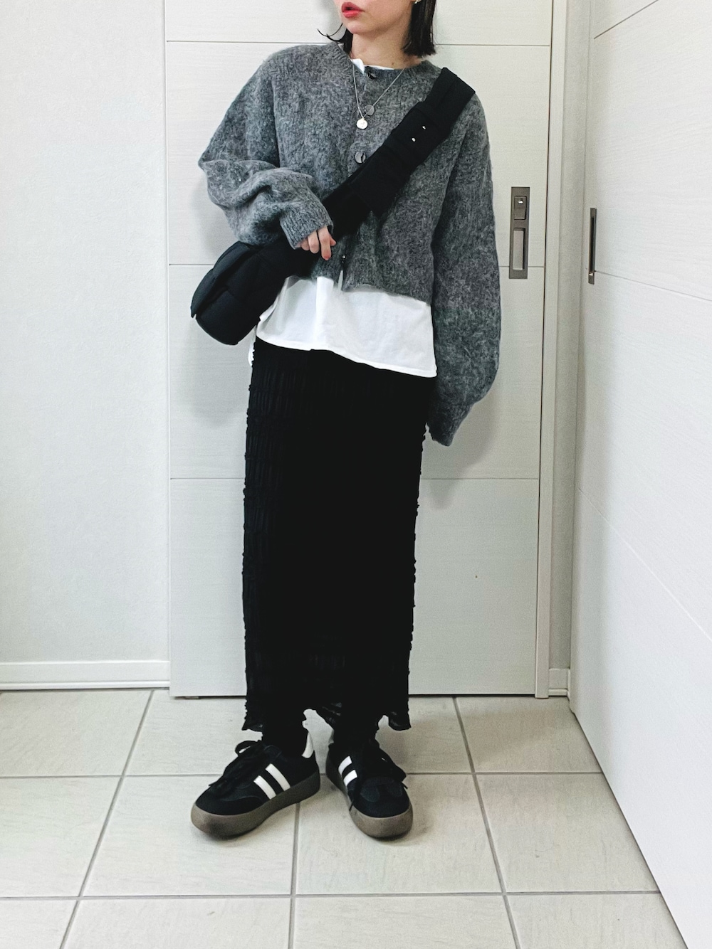 グレー系のカーディガン/ボレロ、ホワイト系のTシャツ/カットソー、ブラック系のスカートを着用したレディースの冬コーディネートの1枚目の写真