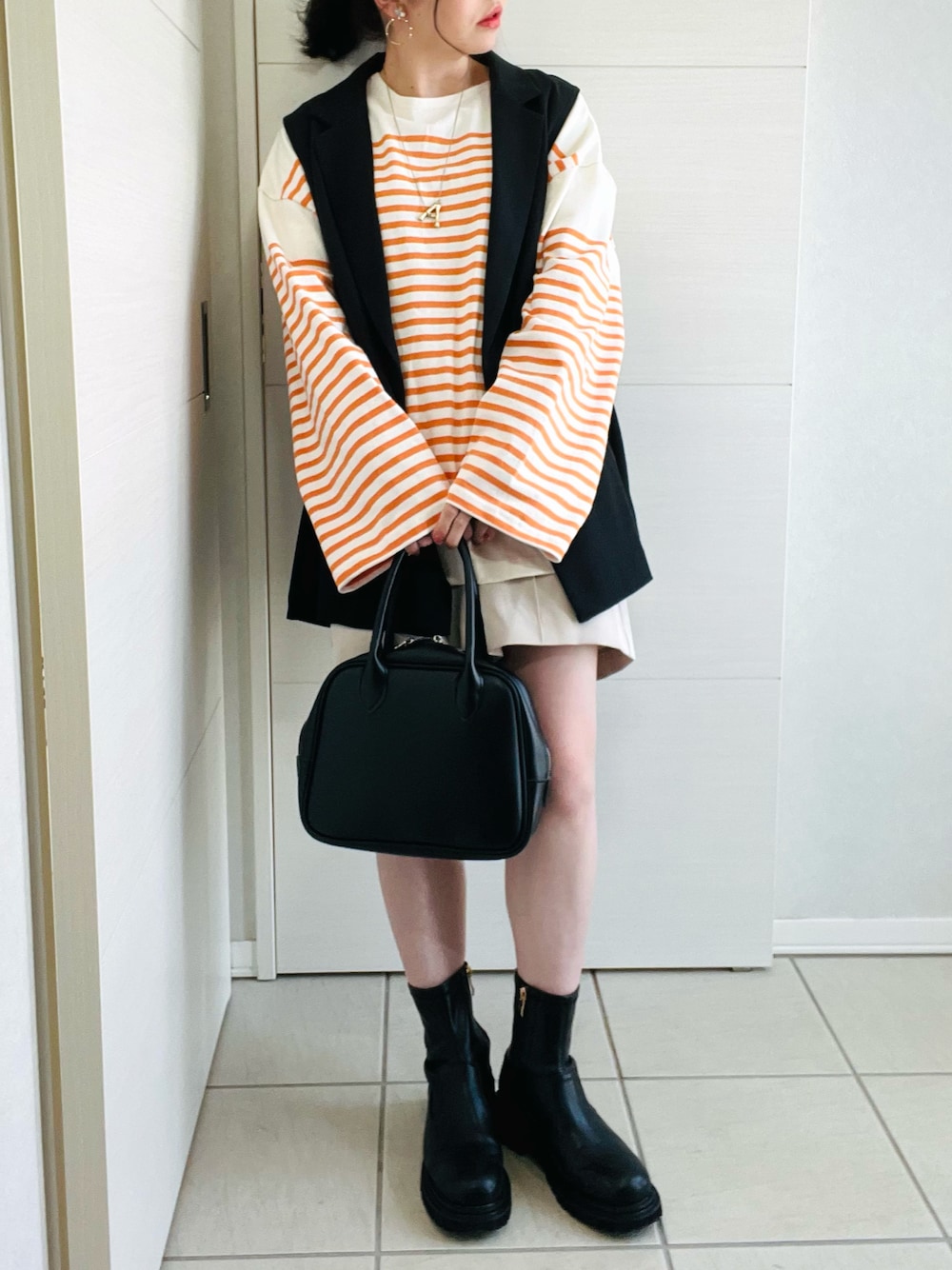 オレンジ系のTシャツ/カットソー、ブラック系のベスト、ホワイト系のスラックスを着用したレディースの春コーディネートの1枚目の写真