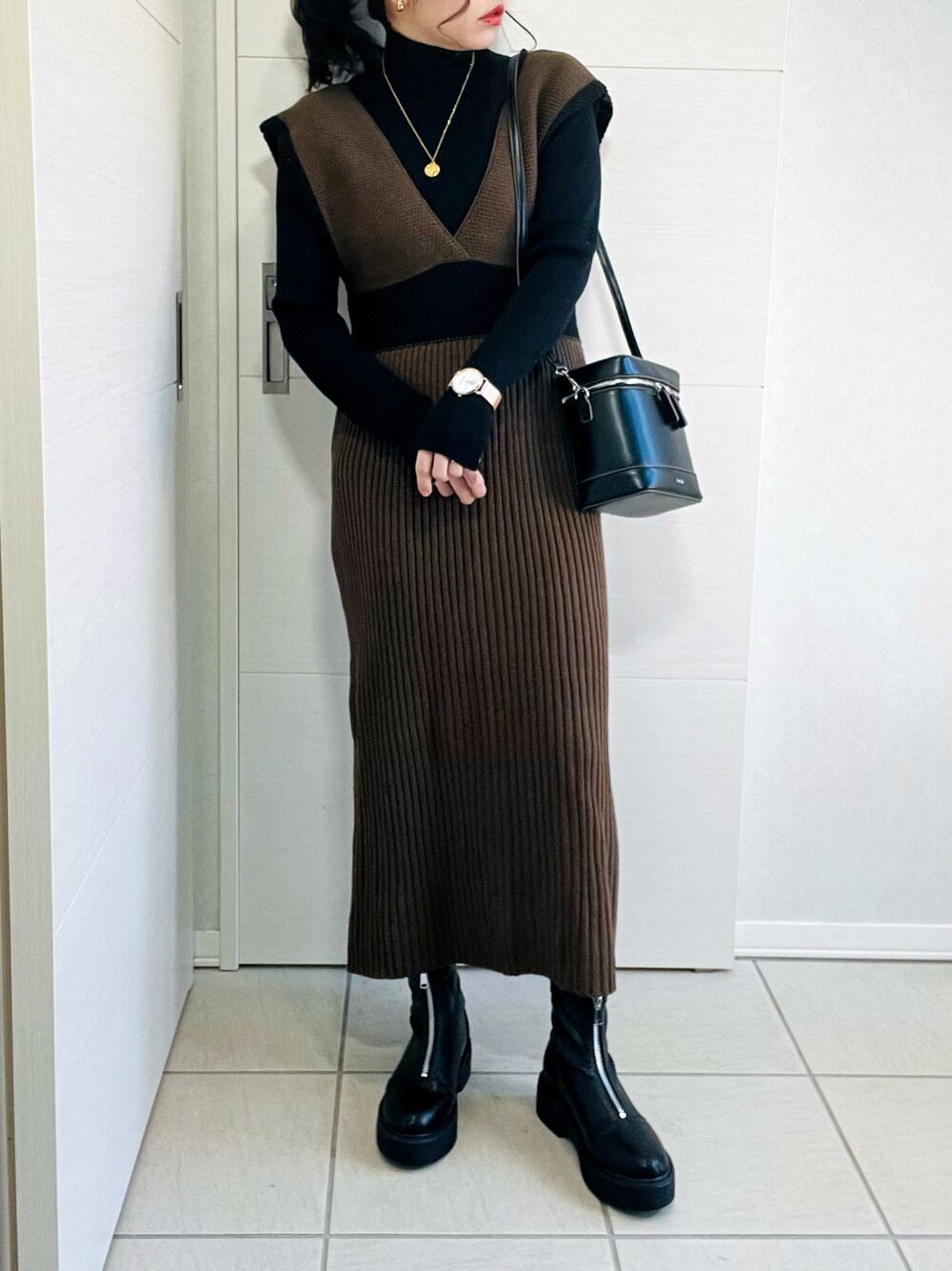 ブラック系のニット/セーター、ブラウン系のワンピース、ブラック系のブーツを着用したレディースの冬コーディネートの1枚目の写真