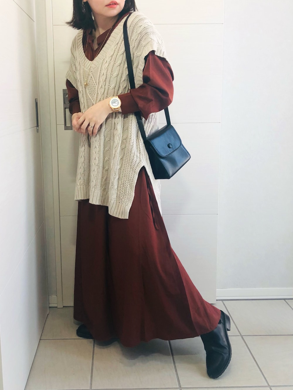 ブラウン系のワンピース、ホワイト系のベスト、ブラック系のブーツを着用したレディースの秋コーディネートの1枚目の写真