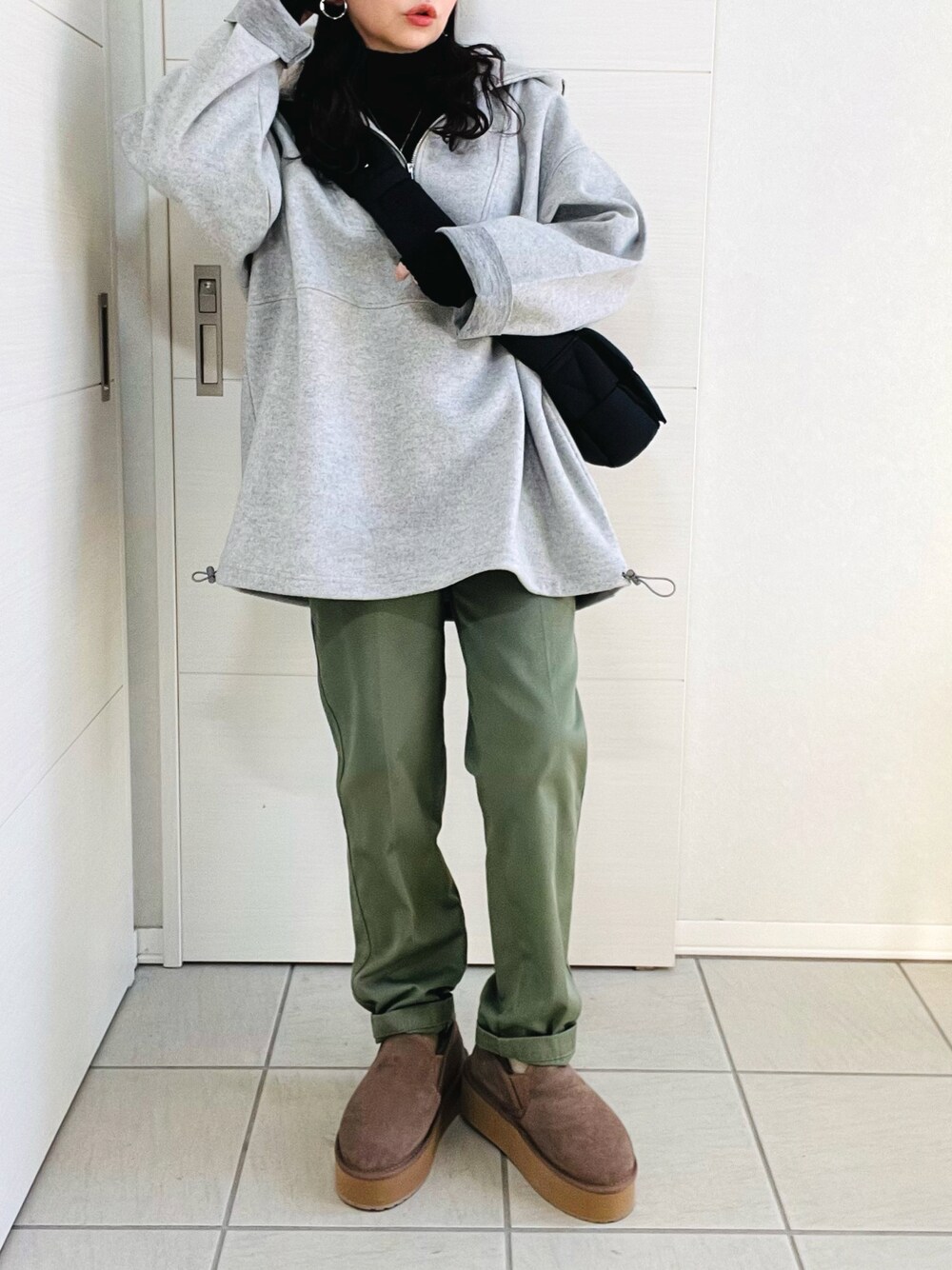 グレー系のパーカー、ブラック系のニット/セーター、グリーン系のチノパンツを着用したレディースの冬コーディネートの1枚目の写真