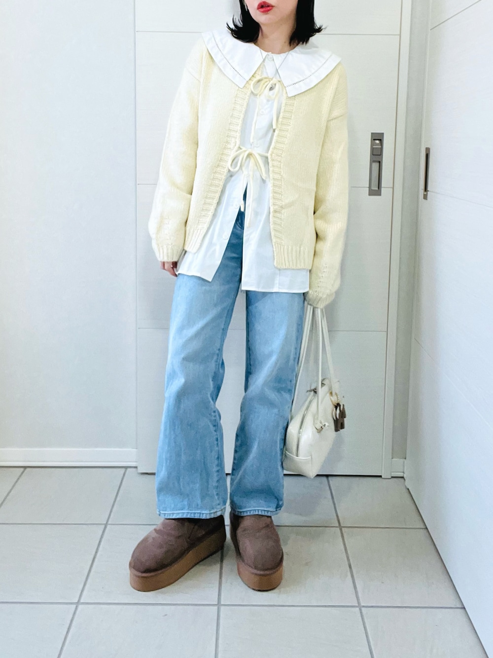 ホワイト系のカーディガン/ボレロ、ホワイト系のシャツ/ブラウス、ブルー系のデニムパンツを着用したレディースの冬コーディネートの1枚目の写真