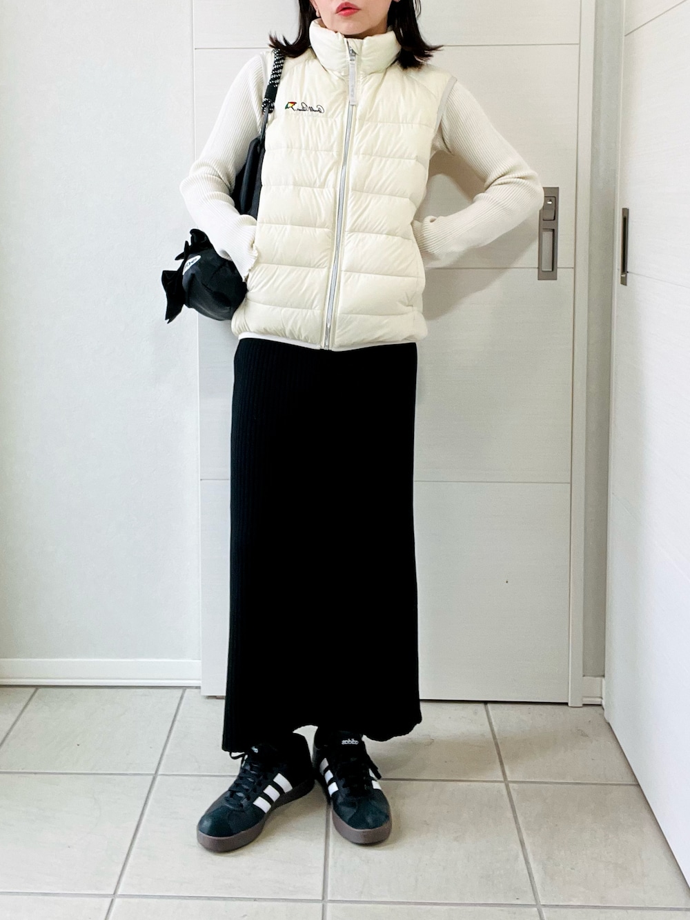 ホワイト系のダウンベスト、ホワイト系のニット/セーター、ブラック系のスカートを着用したレディースの秋コーディネートの1枚目の写真