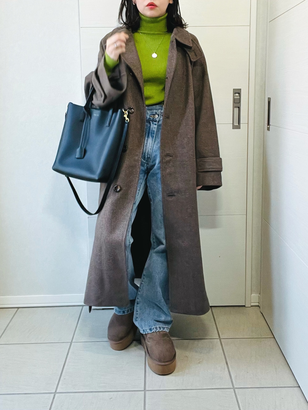 ブラウン系のステンカラーコート、グリーン系のニット/セーター、ブルー系のデニムパンツを着用したレディースの冬コーディネートの1枚目の写真