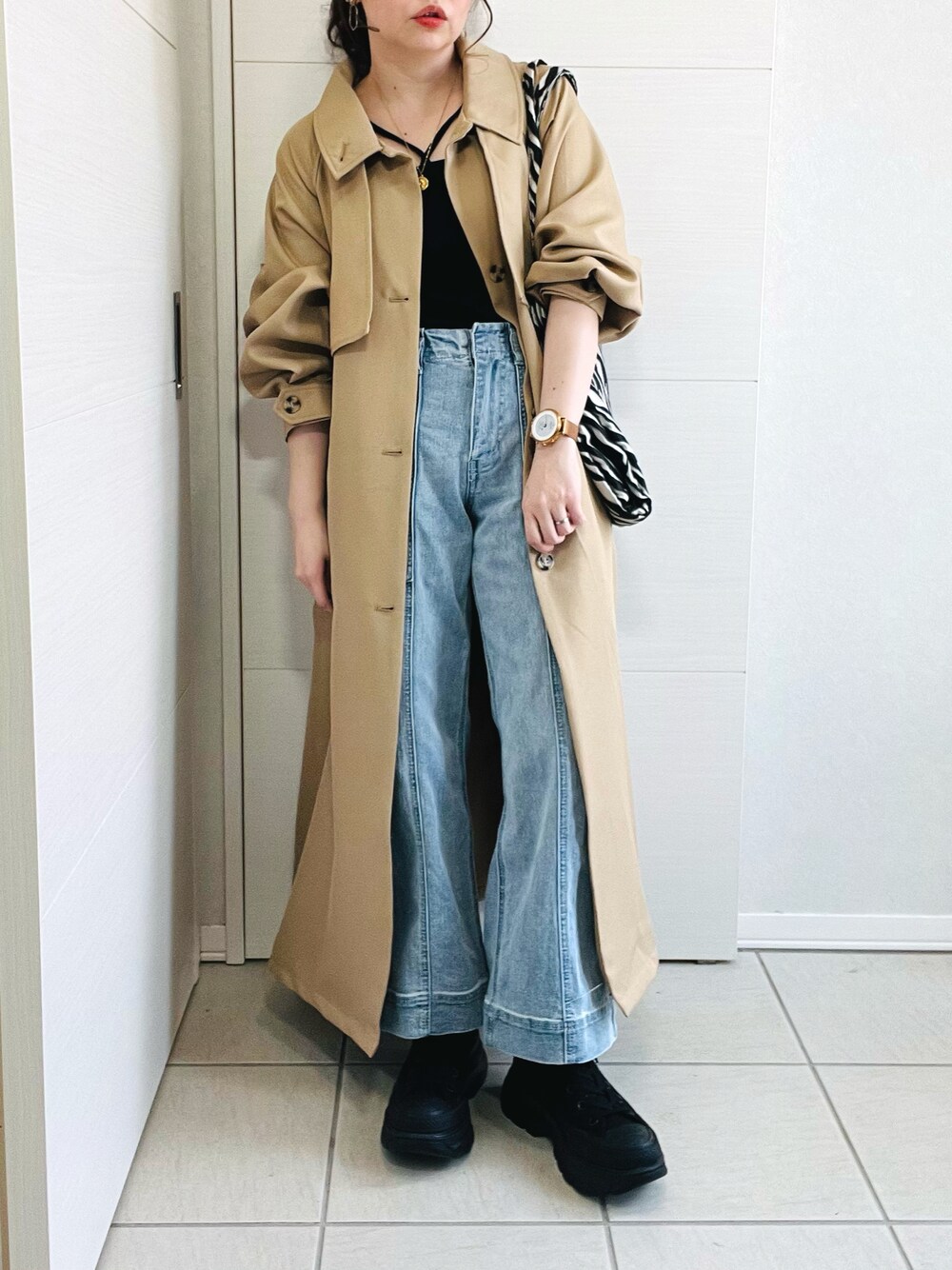 ベージュ系のトレンチコート、ブラック系のキャミソール、ブルー系のデニムパンツを着用したレディースの春コーディネートの1枚目の写真