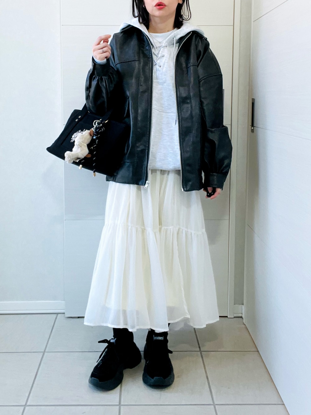 ブラック系のブルゾン、グレー系のパーカー、ホワイト系のスカートを着用したレディースの冬コーディネートの1枚目の写真