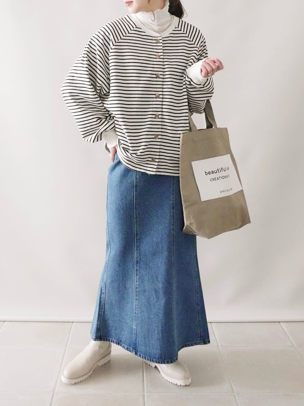 ホワイト系のトップス、ブルー系のデニムスカート、ベージュ系のブーツを着用したレディースの冬コーディネートの1枚目の写真