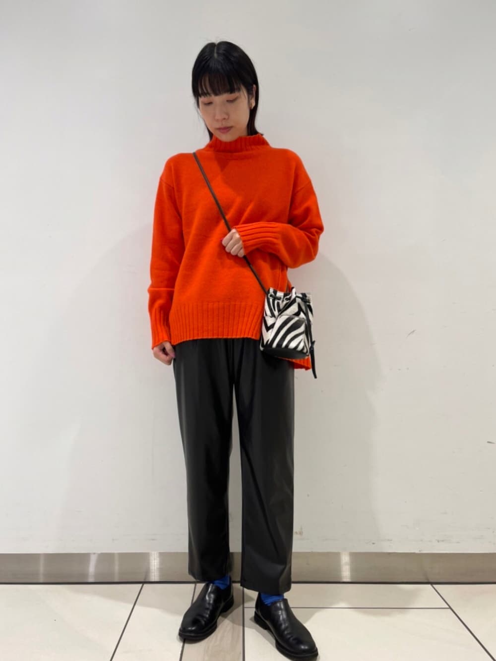 オレンジ系のニット/セーター、ブラック系のショルダーバッグ、ブラック系のその他パンツを着用したレディースの秋コーディネートの1枚目の写真