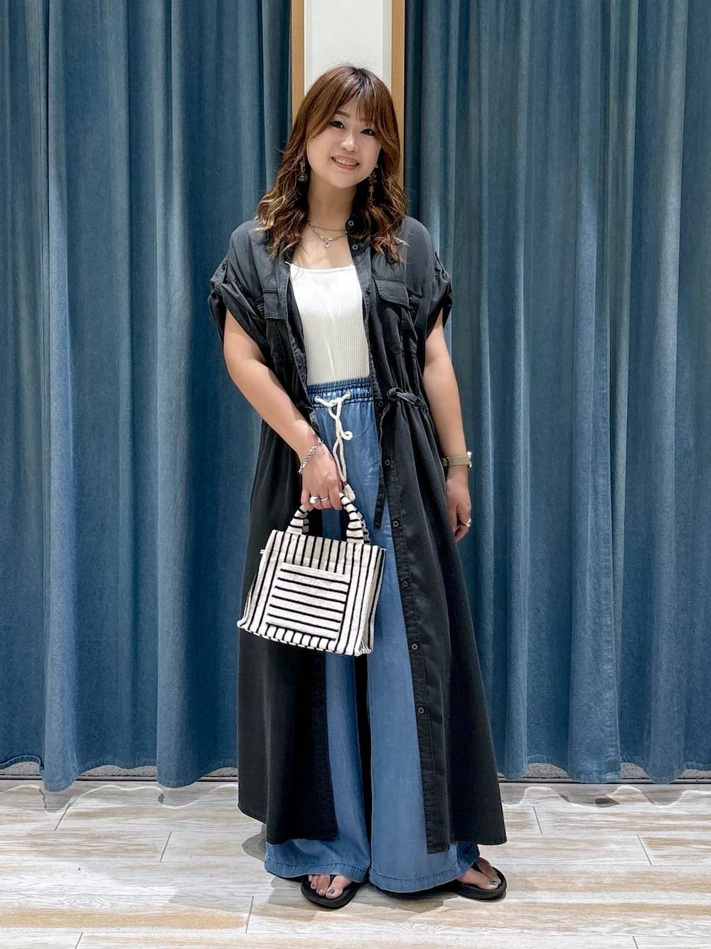 ブルー系のデニムパンツ、ブラック系のサンダル、ベージュ系のトートバッグを着用したレディースの夏コーディネートの1枚目の写真