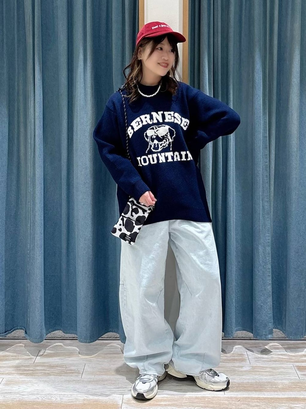 ブルー系のニット/セーター、ブルー系のデニムパンツ、レッド系のキャップを着用したレディースの冬コーディネートの1枚目の写真