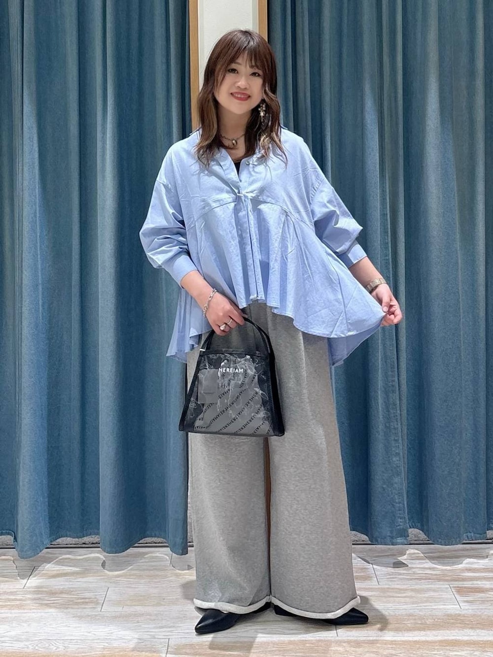 ブラック系のハンドバッグ、ブラック系のパンプス、ブルー系のシャツ/ブラウスを着用したレディースの春コーディネートの1枚目の写真