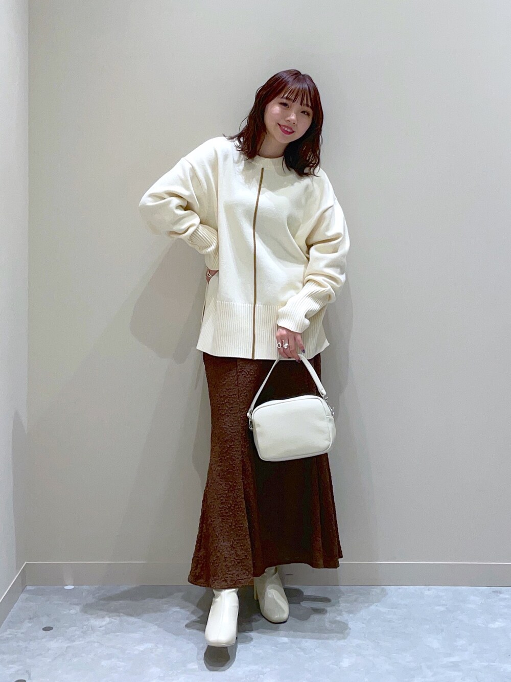 ホワイト系のニット/セーター、ブラウン系のスカート、ホワイト系のブーツを着用したレディースの冬コーディネートの1枚目の写真