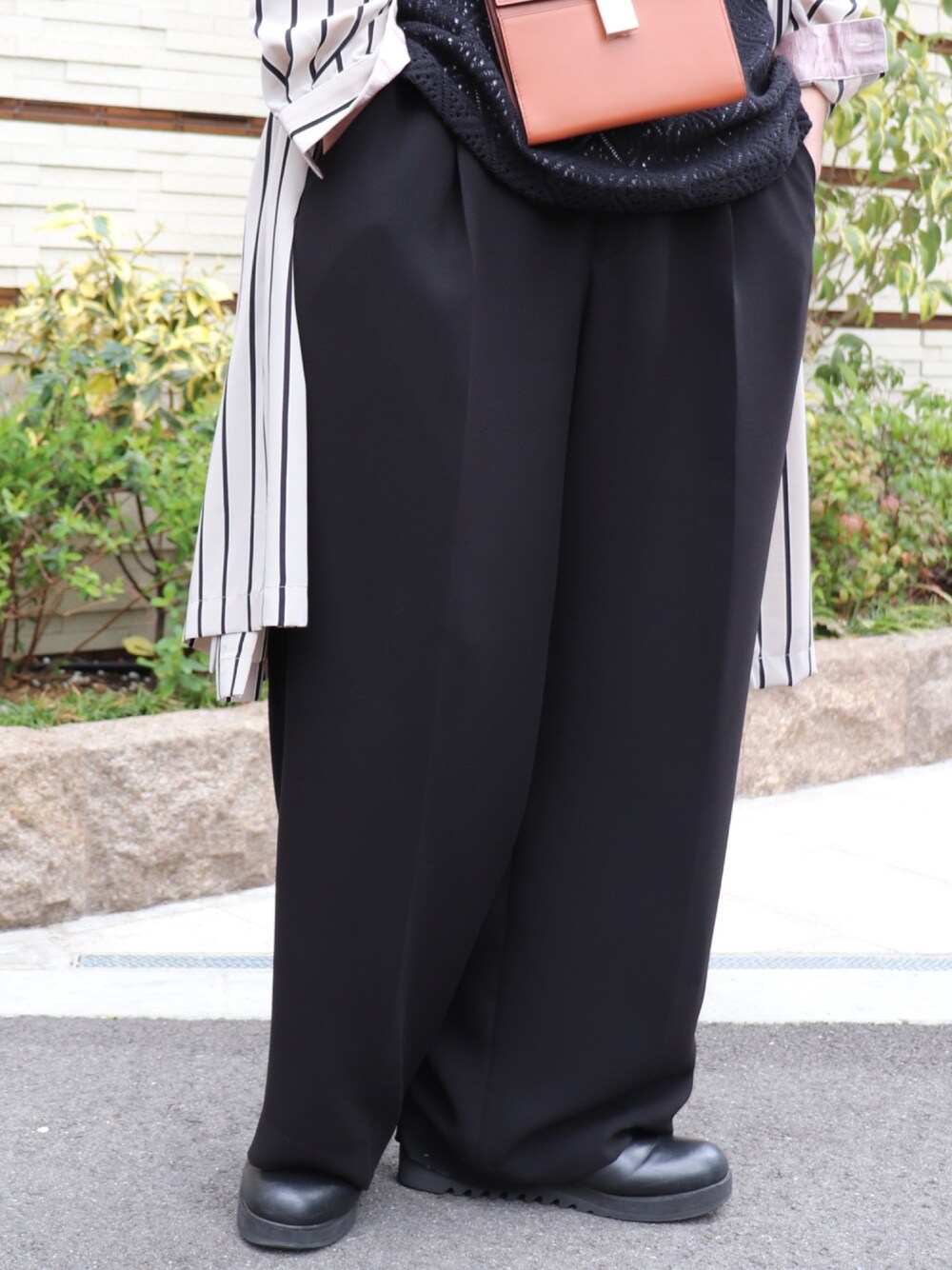 ブラウン系のショルダーバッグ、ブラック系のトップス、ブラック系のスラックスを着用したメンズの春コーディネートの5枚目の写真