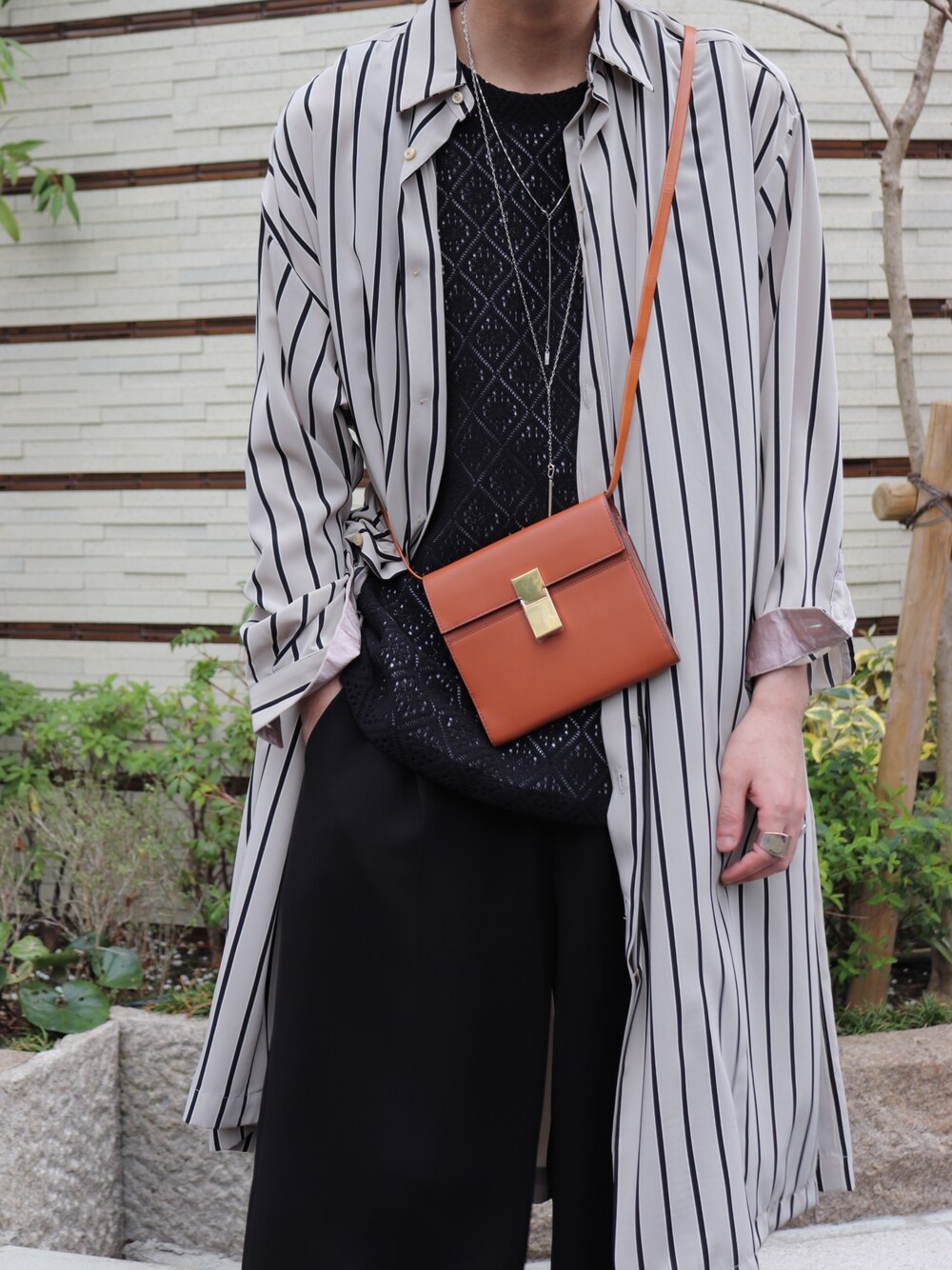 ブラウン系のショルダーバッグ、ブラック系のトップス、ブラック系のスラックスを着用したメンズの春コーディネートの3枚目の写真