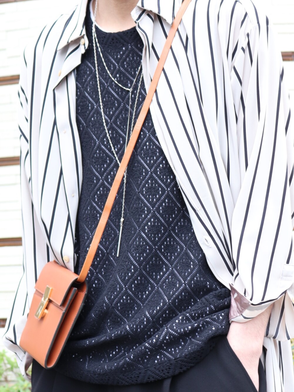 ブラウン系のショルダーバッグ、ブラック系のトップス、ブラック系のスラックスを着用したメンズの春コーディネートの4枚目の写真